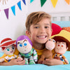 Child holding Buzz Lightyear, Woody, and other plush toys on a bed with colorful pillows and flags.